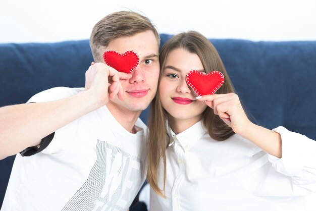Couple holding small toy hearts at faces