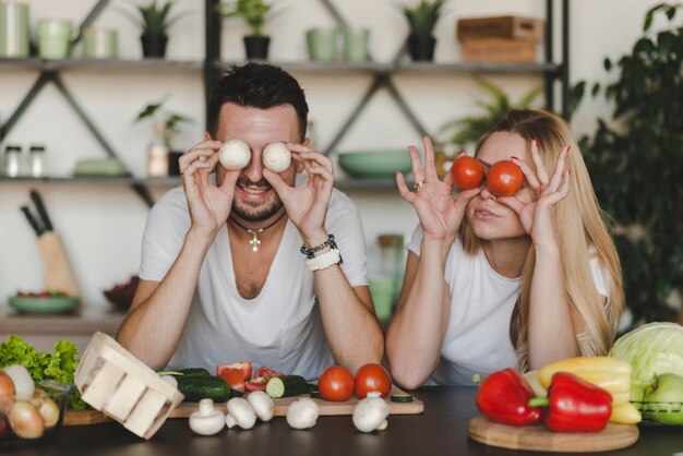 Couple holding whole vegetables over eyes in the kitchen