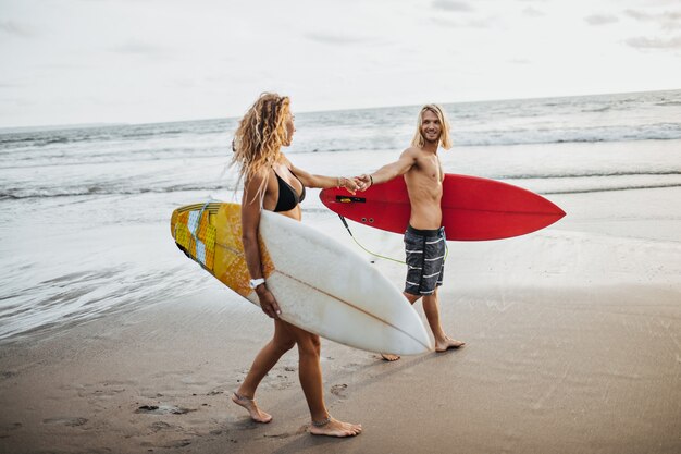 Couple holds hands and gently looks at each other. Man and woman posing with surfboards