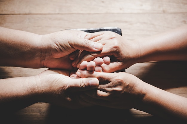 Free photo couple of husband and wife are holding hands and pray together on wooden table with copy space for your text