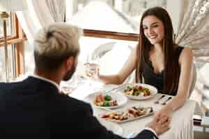 Foto gratuita la coppia sta bevendo vino bianco durante la cena romantica al ristorante e si tiene per mano