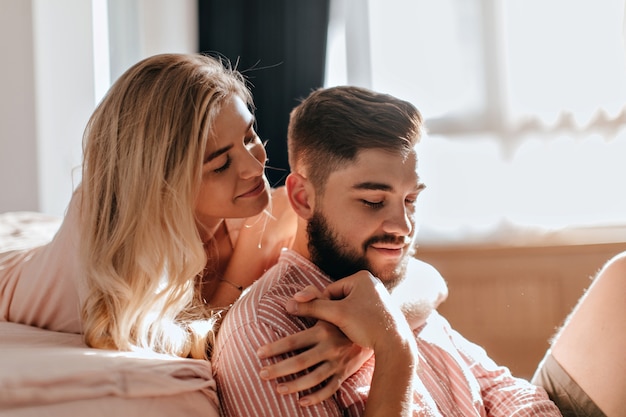 Couple is resting in bedroom. Lovers girl and boy hugging in sunny room with tenderness.