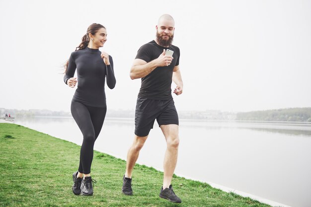 Couple jogging and running outdoors in park near the water. Young bearded man and woman exercising together in morning