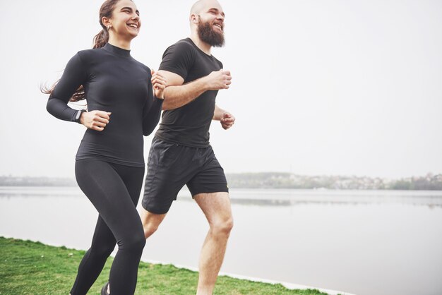 Couple jogging and running outdoors in park near the water. Young bearded man and woman exercising together in morning