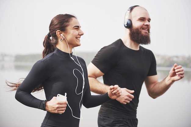 Couple jogging and running outdoors in park near the water. Young bearded man and woman exercising together in morning