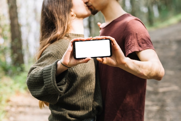 カップルがキスをし、自然の中でスマートフォンテンプレートを表示