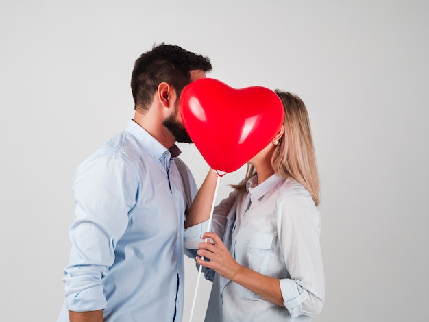 Free photo couple kissing behind balloon for valentines