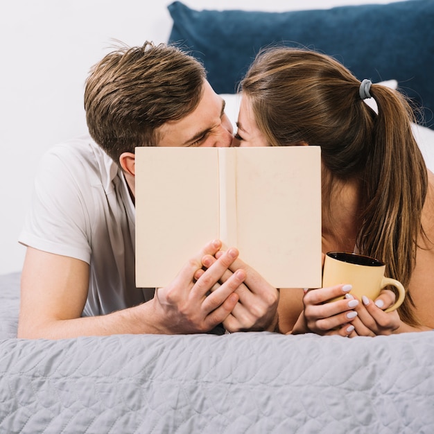 Couple kissing covering faces on bed 