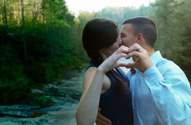 Пара целуется и делает сердечко руками в окружении зелени и водопада