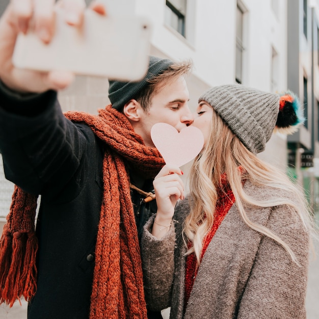 Free photo couple kissing behind heart and taking selfie