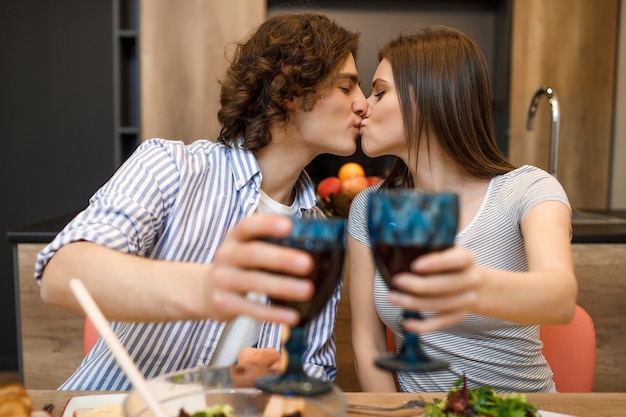 ワイングラスと自宅のキッチンでキスするカップル