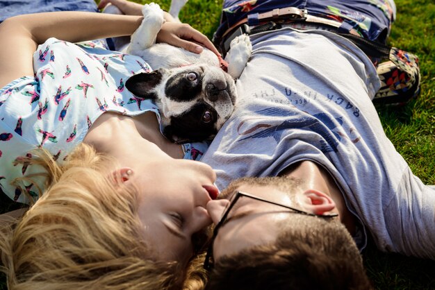カップルがキス、フレンチブルドッグと公園の芝生の上で横になっています。