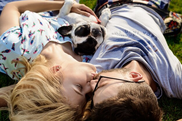 Couple kissing, lying with French bulldog on grass in park