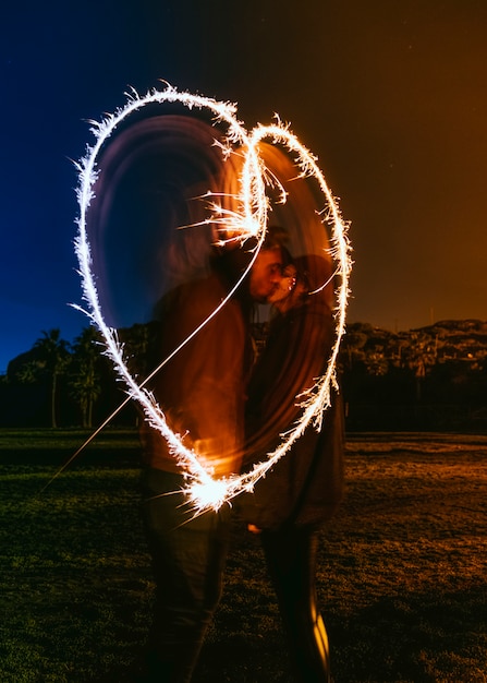 Free photo couple kissing near heart drawing from sparklers in dark street