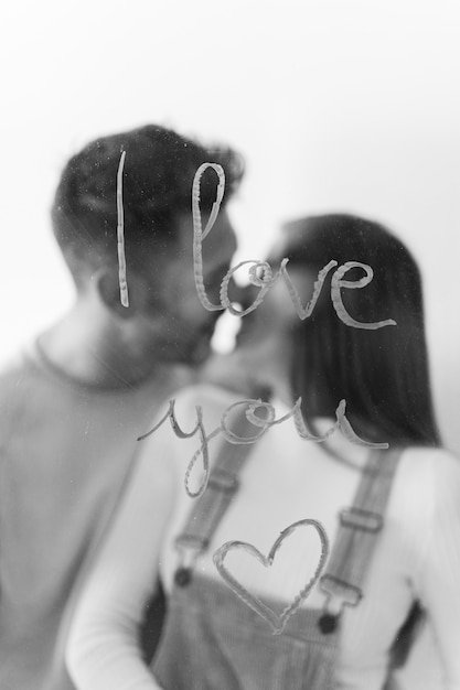 Couple kissing near I love you inscription on glass 