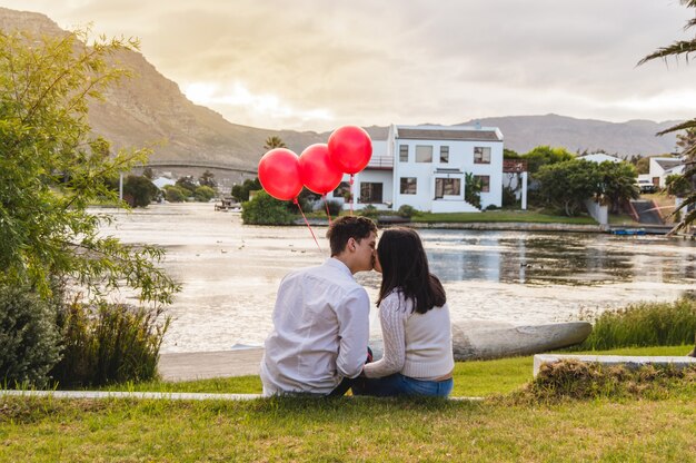 Couple kissing in a park with red balloons