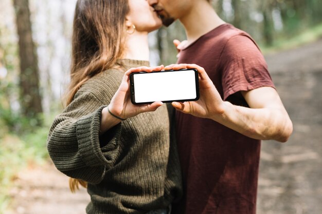 Couple kissing and showing smartphone template in nature