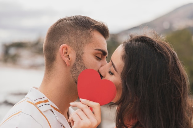 Free photo couple kissing with paper heart shape