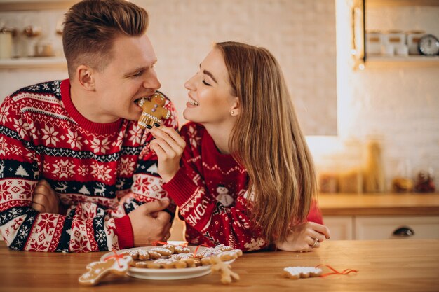 クリスマスのクッキーの男を食べるキッチンでカップル