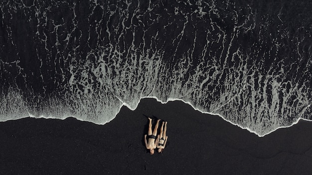 Free photo couple lie on a black sand near ocean