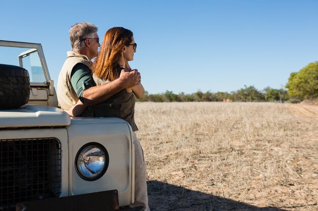 Couple looking away while standing by off road vehicle on field