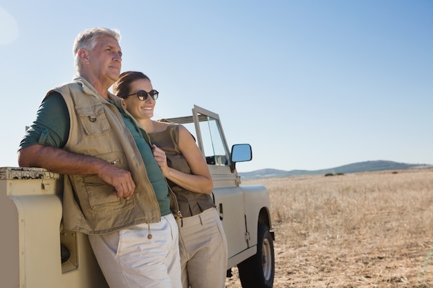 Couple looking away while standing by vehicle on field
