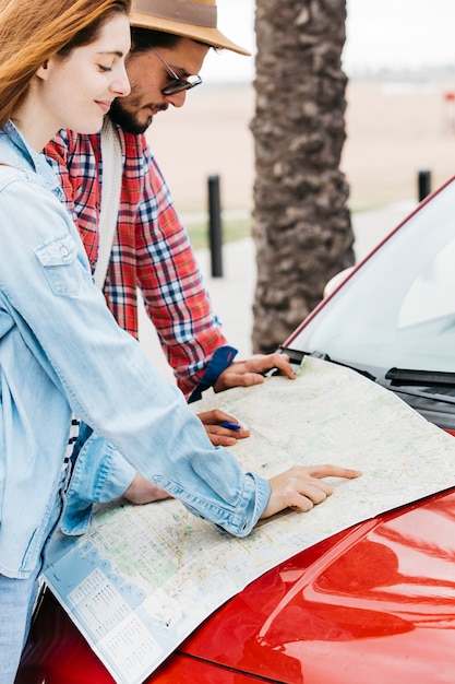 Couple looking at road map on red car