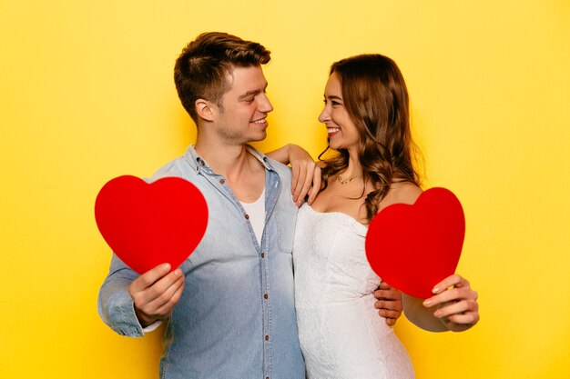 Couple in love celebrating St. Valentine's day, holding red hearts, looking to each other.