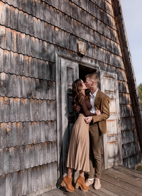 Couple in love dressed in casual clothes is kissing near the front door of a wooden building outdoors