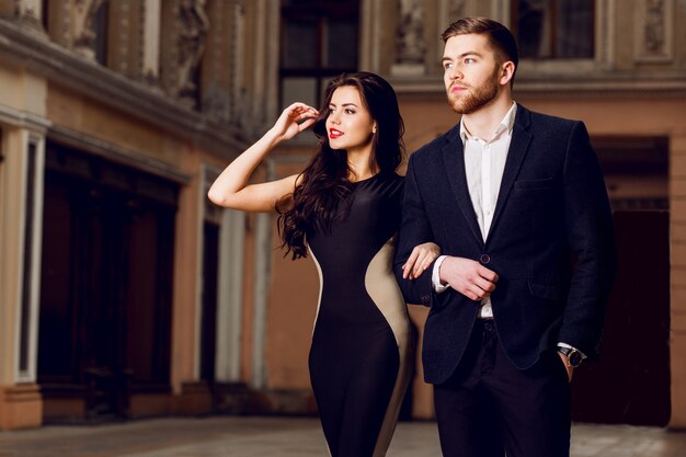 Couple in love in   elegant outfit walking in old town street . Pretty brunette woman with red lips and her handsome boyfriend have time off.