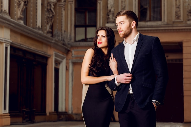 Couple in love in   elegant outfit walking in old town street . Pretty brunette woman with red lips and her handsome boyfriend have time off.