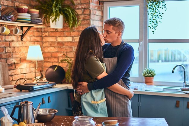 恋をしているカップル。ハンサムな男性は朝、ロフトスタイルのキッチンで彼の妻を抱きしめてキスします。
