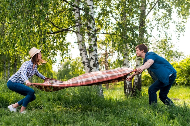Couple in love placing picnic blanket on meadow