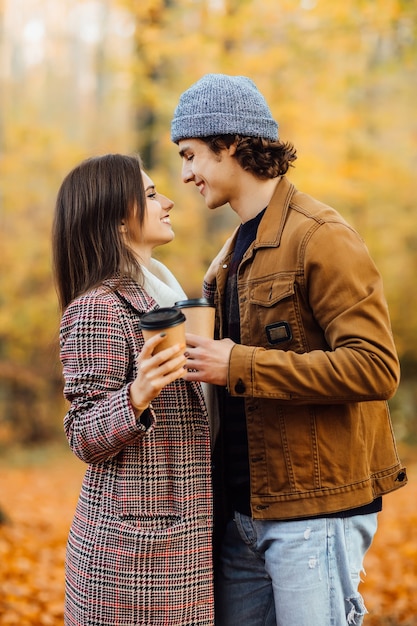 Влюбленная пара в шарфах сидит в парке с чашками чая или кофе