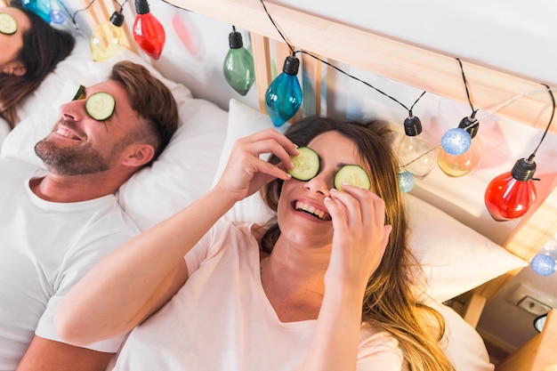 Couple lying on bed with cucumber slice over their eyes