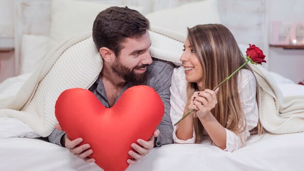 Couple lying on bed with soft red toy heart