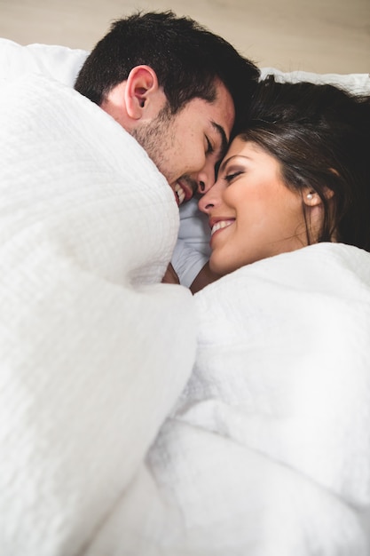 Couple lying in bed and wrapped up to the neck