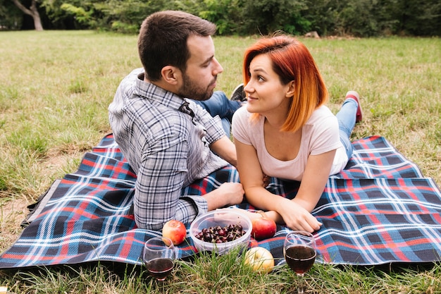 Couple lying on blanket over green grass enjoying fruits