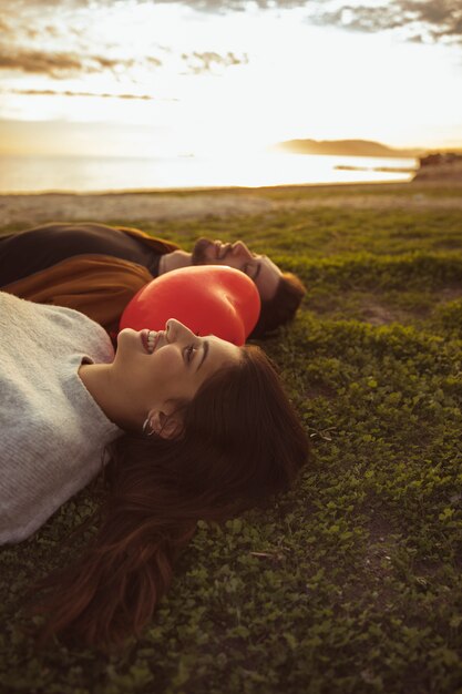 Couple lying on grass with red heart balloon