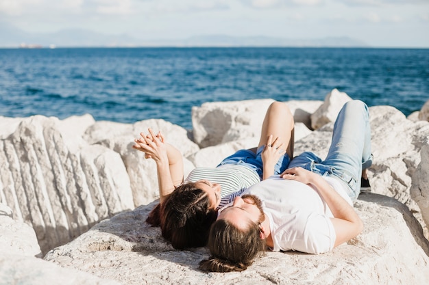 Free photo couple lying on rocks by the sea