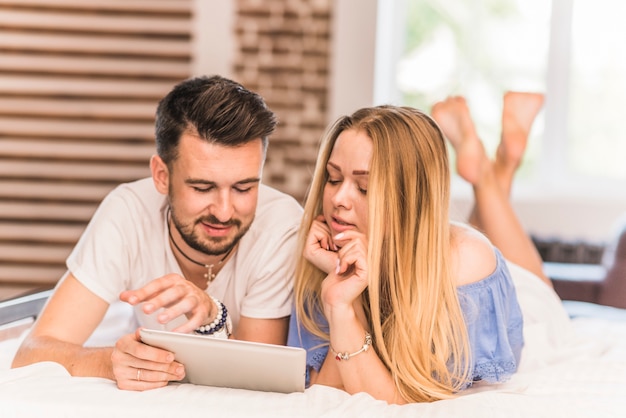 Free photo couple lying together on bed looking at digital tablet