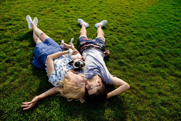 Free photo couple lying with french bulldog on grass in park