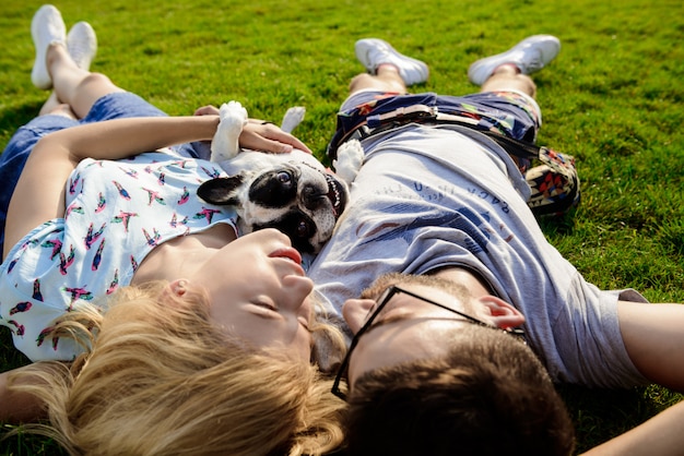 Couple lying with French bulldog on grass in park