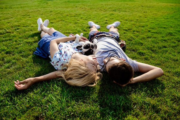 Couple lying with French bulldog on grass in park