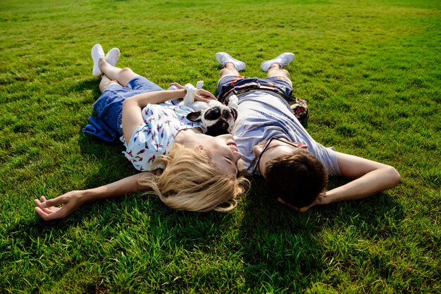 Couple lying with French bulldog on grass in park