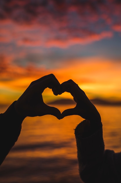 Free photo couple making heart from hands on sea shore