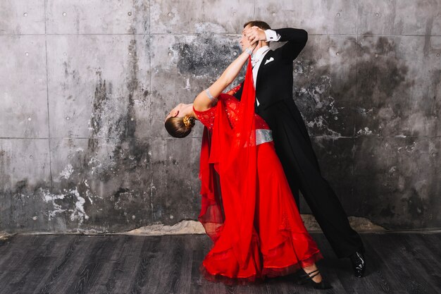 Couple performing dance near gray wall