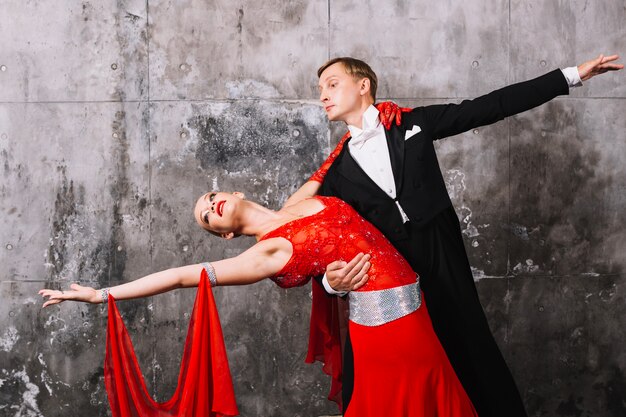 Couple performing dance near gray wall