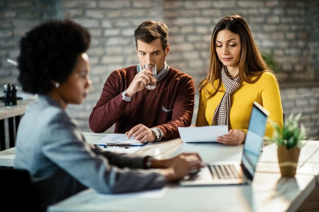 Couple planning their investments and analyzing a contract while their financial advisor in working on laptop during the meeting