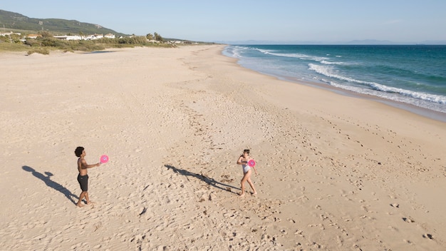 Couple playing badminton on sandy beach by sea